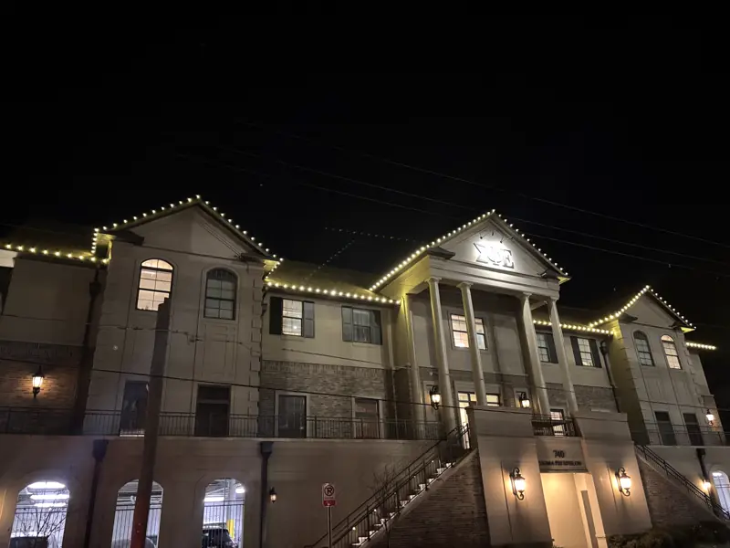 Warm white lights along every roofline of a three-story building